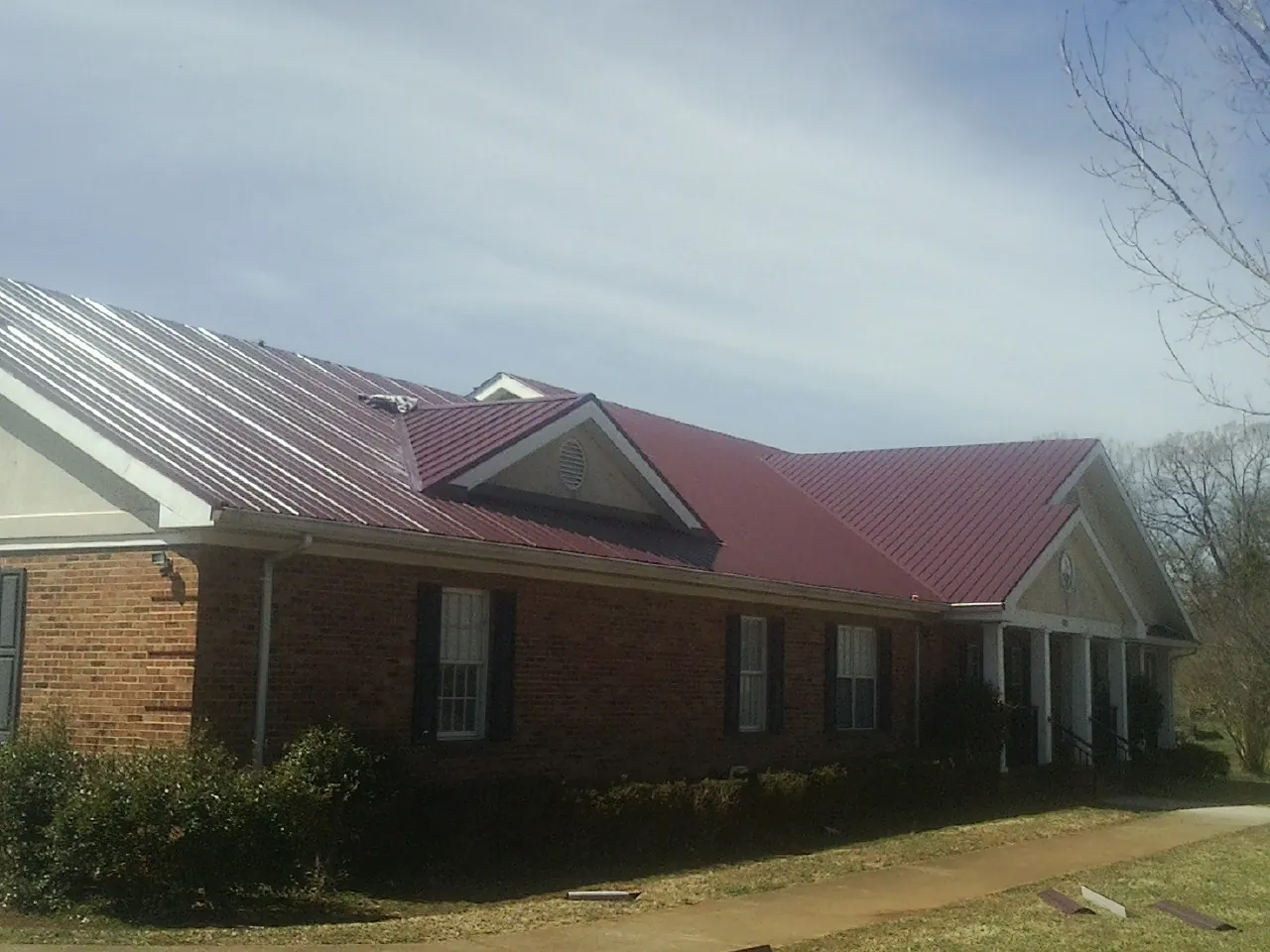 Red metal roof with gabled entries on a long brick building, from a Hail Damage Roof Repair job in Mc Rae Helena
