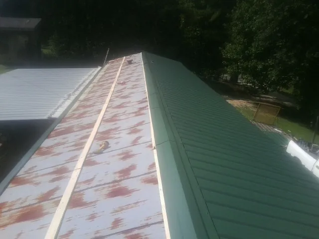 Old rusted panels beside newly installed green metal roofing — Wind Damage Roof Repair by Roofing Brothers in Mc Rae Helena