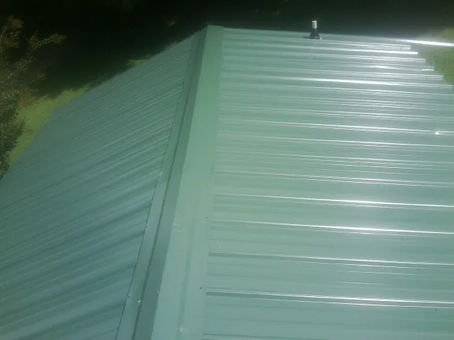 New green metal panels meeting at the ridge of a roof — Flat Roof Repair work by our crew in Mc Rae Helena