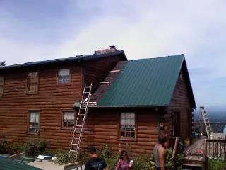 Green metal roof going on a two story log home with ladders set in Mc Rae Helena