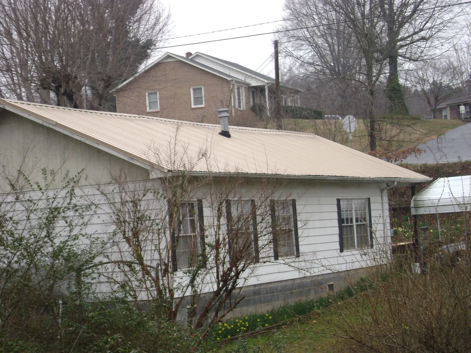 Tan metal roof on a white sided house set into a hillside — Commercial Roofing by Roofing Brothers in Mc Rae Helena